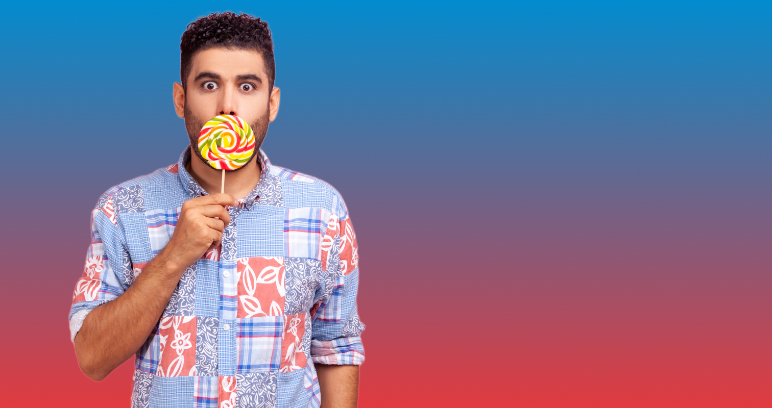 Man with short dark hair in colourful shirt holding a lollipop over his mouth